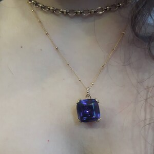 May include: A gold chain necklace with a large, square, purple gemstone pendant.