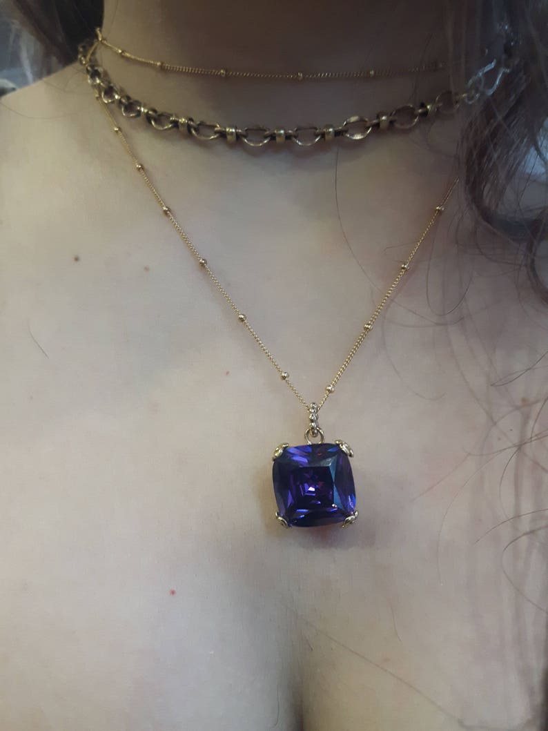 May include: A gold chain necklace with a large, square, purple gemstone pendant.