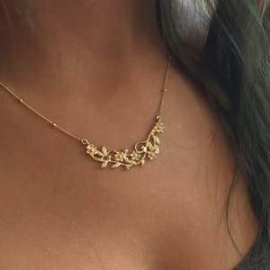 May include: A gold necklace with a delicate floral design. The necklace features a chain with small beads and a pendant shaped like a vine with small flowers.