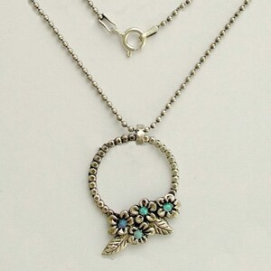 May include: A silver necklace with a circle pendant featuring a cluster of opal flowers. The necklace is made of a delicate ball chain.