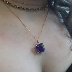 May include: A gold chain necklace with a large, rectangular, purple gemstone pendant.