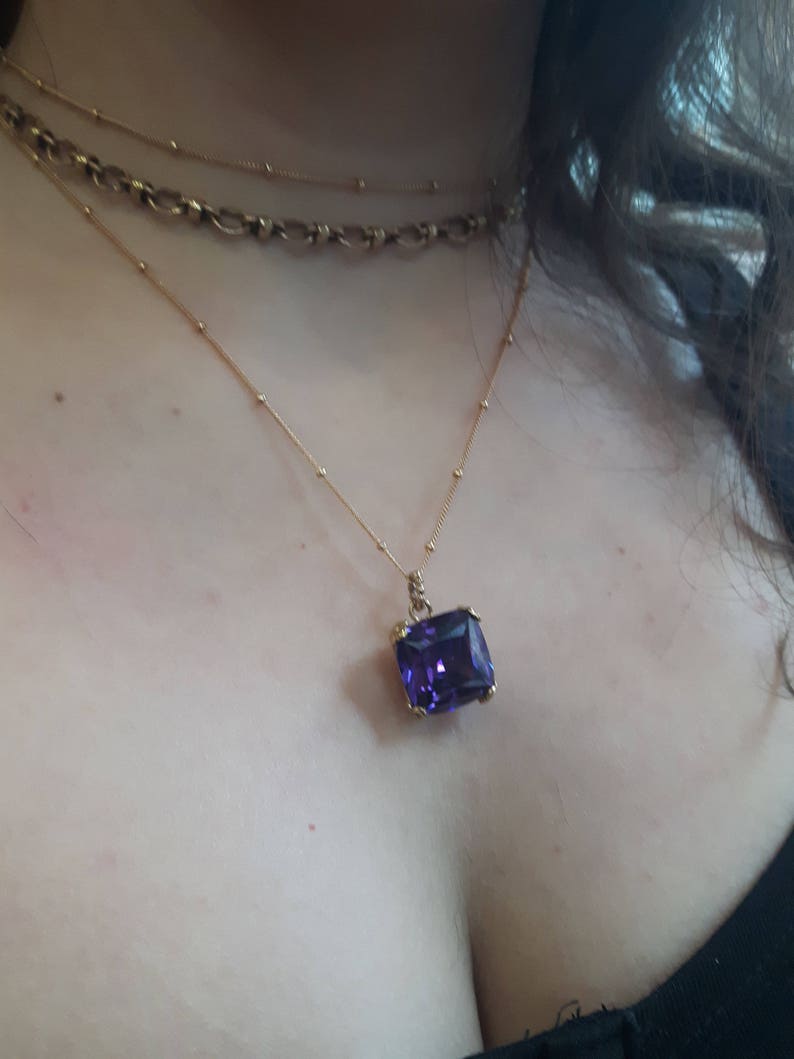 May include: A gold chain necklace with a large, rectangular, purple gemstone pendant.