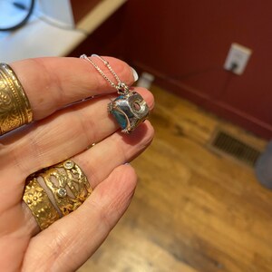 May include: A silver necklace with a blue gemstone pendant. The pendant is a square shape with a textured surface.
