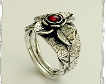 Puede incluir: Un anillo de plata con un diseño de hojas texturizadas y una piedra preciosa roja en el centro de una flor.
