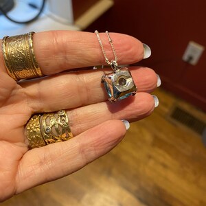 May include: A silver chain necklace with a square pendant featuring a faceted blue gemstone.