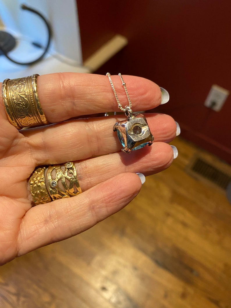 May include: A silver chain necklace with a square pendant featuring a faceted blue gemstone.