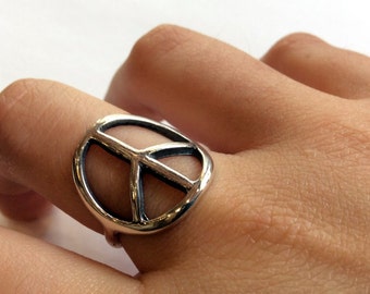 Könnte beinhalten: Ein silberner Friedenszeichenring. Der Ring wird an einem Finger getragen.