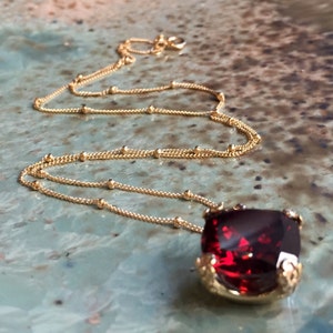 May include: A gold chain necklace with a large, red, square-shaped gemstone pendant.