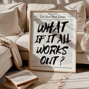 Puede incluir: Un estampado enmarcado con un fondo de periódico, con el titular "The New York Times". El texto negro en negrita dice "WHAT IF IT ALL WORKS OUT?" El estampado está en un marco de madera clara, apoyado contra un sofá beige.