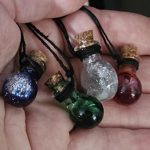 May include: Four small glass bottle pendants with cork stoppers, each filled with a different colored liquid and glitter. The bottles are suspended on black cords. Colors include blue, green, silver, and red.