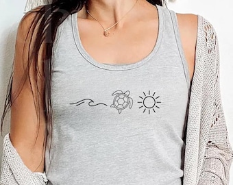 Può includere: Canotta grigio chiaro con un disegno a tratto nero di un'onda, una tartaruga e un sole. La canotta è abbinata a una cintura marrone e jeans blu. Un cardigan grigio chiaro è drappeggiato sulle spalle.