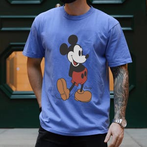 Op de afbeelding: Een blauw T-shirt met een vintage Mickey Mouse-afbeelding en het woord "Disney" gedrukt in de rechterbenedenhoek.