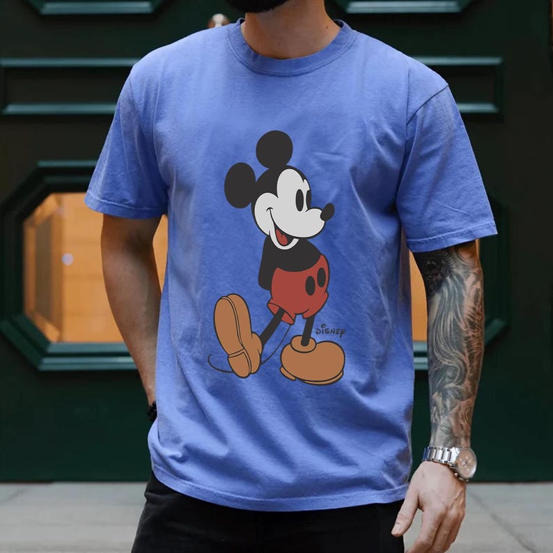 Op de afbeelding: Een blauw T-shirt met een vintage Mickey Mouse-afbeelding en het woord "Disney" gedrukt in de rechterbenedenhoek.