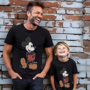Op de afbeelding: Een zwart T-shirt met een vintage Mickey Mouse-print. Een bijpassend zwart T-shirt met een vintage Mickey Mouse-print wordt gedragen door een kind.