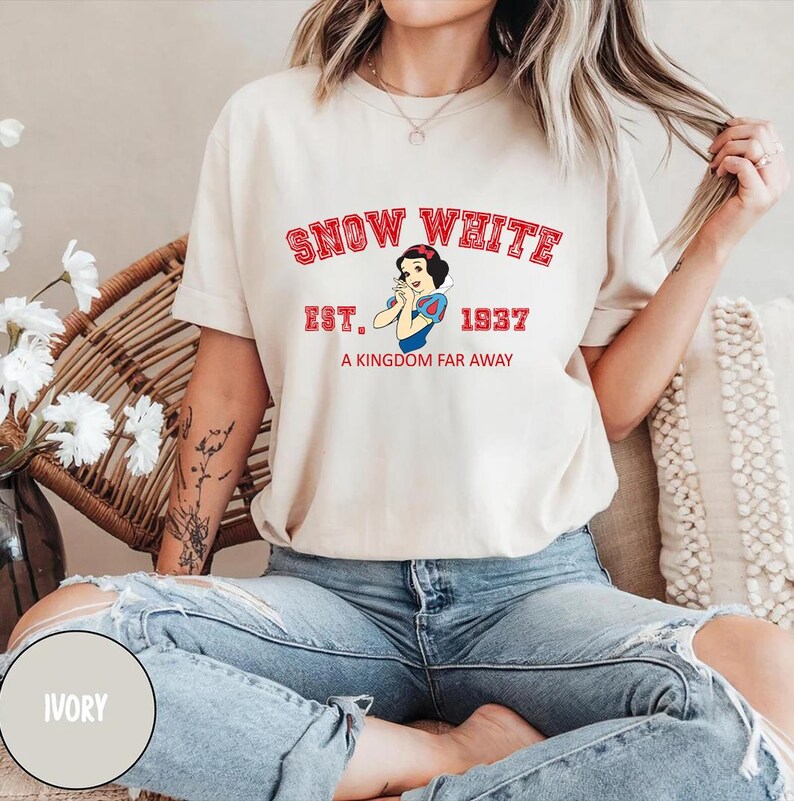 May include: Ivory t-shirt with a graphic print of Snow White from the Disney movie Snow White and the Seven Dwarfs. The graphic includes the text "Snow White", "Est. 1937", and "A Kingdom Far Away".