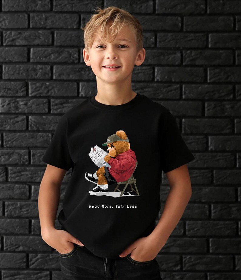 May include: A black t-shirt with a graphic of a cartoon bear wearing a baseball cap and sunglasses, sitting in a chair and reading a newspaper. The text "Read More, Talk Less" is printed below the graphic.