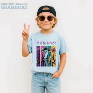 May include: A light blue t-shirt with the text "SATA BOYS" and a graphic of six anime-style characters in vertical color blocks. The shirt is made of Comfort Colors Chambray fabric.