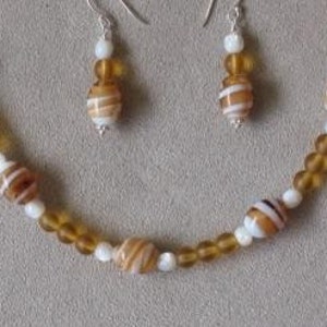 May include: A necklace and earring set featuring a mix of amber and white beads. The necklace has larger, striped beads interspersed with smaller amber and white beads. The earrings mirror the design with smaller versions of the striped beads.