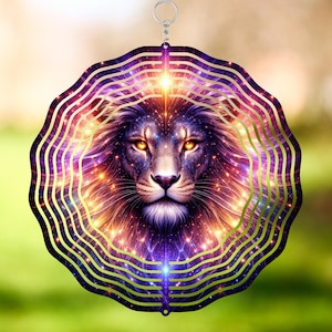 May include: A decorative wind spinner featuring a detailed lion's face with a cosmic design. The lion has glowing orange eyes and a purple and gold mane, surrounded by concentric gold lines. The background is a blurred green.
