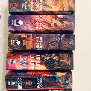 Pu&ograve; includere: Una pila di libri tascabili con copertine rosso, bianco e blu. I libri fanno tutti parte della serie La Ruota del Tempo di Robert Jordan. I titoli dei libri sono: La Grande Caccia, Il Drago Rinato, L'Ascesa delle Ombre, I Fuochi del Cielo, Signore del Caos, Il Sentiero delle Daga e Cuore d'Inverno.