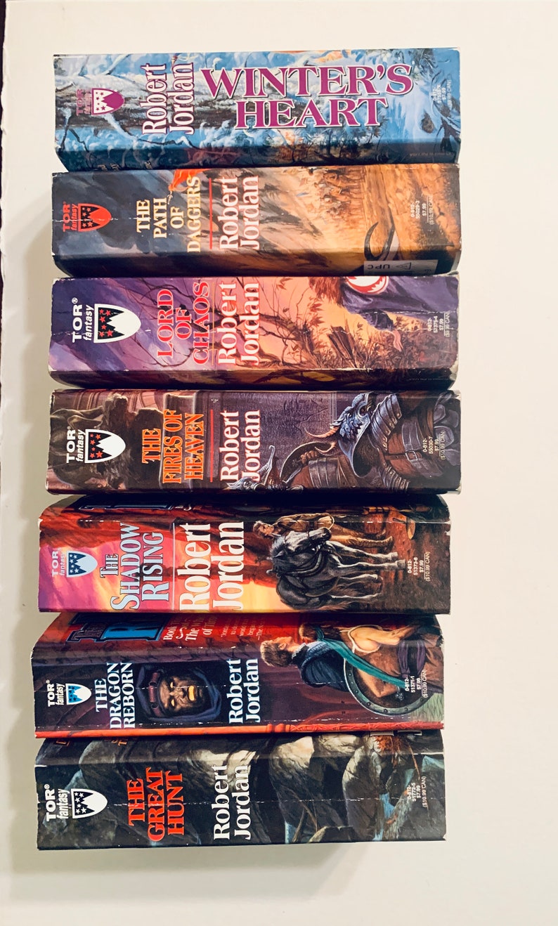 Pu&ograve; includere: Una pila di libri tascabili con copertine rosso, bianco e blu. I libri fanno tutti parte della serie La Ruota del Tempo di Robert Jordan. I titoli dei libri sono: La Grande Caccia, Il Drago Rinato, L'Ascesa delle Ombre, I Fuochi del Cielo, Signore del Caos, Il Sentiero delle Daga e Cuore d'Inverno.