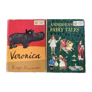 May include: Two vintage children's books. The book on the left is titled "Veronica" by Roger Duvoisin. It features a red cover with a cartoon illustration of a hippopotamus. The book on the right is titled "Andersen's Fairy Tales". It features a green cover with illustrations of fairy tale characters.