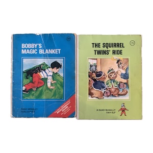 May include: Two vintage children's books with colorful covers. The book on the left is titled "Bobby's Magic Blanket" and the book on the right is titled "The Squirrel Twins' Ride". Both books are published by Rand McNally.