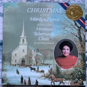 May include: A Christmas album cover featuring a snowy winter scene with a church, a horse-drawn carriage, and people walking. The album title is "Christmas with Marilyn Horne and the Mormon Tabernacle Choir" with the director's name, Jerold Ottley, listed below.