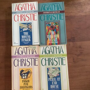 May include: Four paperback books by Agatha Christie, all featuring the author's name and the words "Mystery's #1 Bestseller" on the cover. The titles are "The Moving Finger", "The Harlequin Tea Set", "Parker Pyne Investigates", and "Peril at End House".