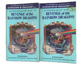May include: Two vintage "Dungeons & Dragons" adventure books titled "Revenge of the Rainbow Dragons." The covers are light blue with a fantasy illustration of a dragon, a person, and a rainbow. The text includes "An Endless Quest Book #6" and the author's name, Rose Estes.