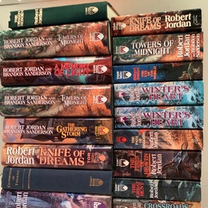 Pu&ograve; includere: Una pila di 14 romanzi fantasy di Robert Jordan e Brandon Sanderson. I libri sono in varie tonalit&agrave; di verde, blu e marrone con lettere dorate. I titoli includono "Knife of Dreams", "Towers of Midnight", "A Memory of Light", "The Gathering Storm", "Winter's Heart", "The Fires of Heaven", "The Great Hunt" e "Crossroads of Twilight".