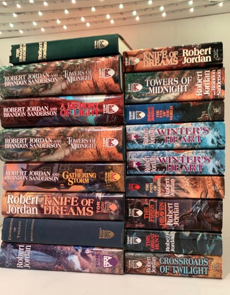 Pu&ograve; includere: Una pila di 14 romanzi fantasy di Robert Jordan e Brandon Sanderson. I libri sono in varie tonalit&agrave; di verde, blu e marrone con lettere dorate. I titoli includono "Knife of Dreams", "Towers of Midnight", "A Memory of Light", "The Gathering Storm", "Winter's Heart", "The Fires of Heaven", "The Great Hunt" e "Crossroads of Twilight".