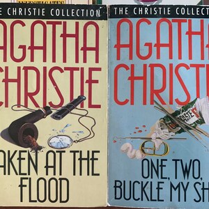 May include: Two paperback books from The Christie Collection featuring Agatha Christie novels. The book on the left is titled "Taken at the Flood" and features a pipe and a pocket watch on a yellow background. The book on the right is titled "One, Two, Buckle My Shoe" and features a blue background with a tube of toothpaste, a toothbrush, and a dental mirror.