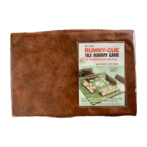 May include: A brown leatherette game board case with a clear plastic window showing the game board and tiles for the De Luxe Rummy-Cue Tile Rummy Game. The game board is green with white tiles and four 2-tier racks.