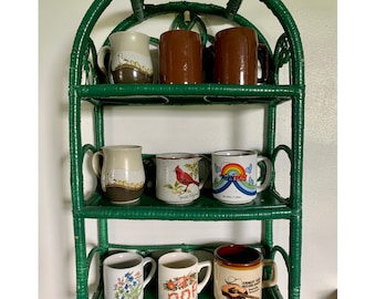 May include: A green wicker shelf unit with three shelves holds ten ceramic mugs. The mugs have various designs, including birds, flowers, and a cardinal.