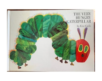 May include: A hardcover children's book titled "The Very Hungry Caterpillar" by Eric Carle. The cover features a colorful illustration of a green caterpillar with a red head and large yellow eyes. The book is on a white background.
