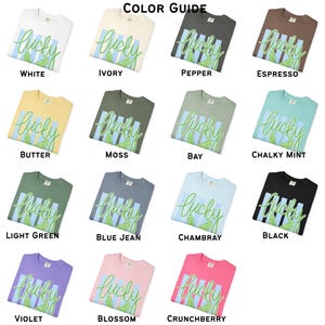 May include: A color guide displays various t-shirts in different colors, each featuring the word "lucky" in a script font with a green leaf design. Colors include white, ivory, pepper, espresso, butter, moss, bay, chalky mint, light green, blue jean, chambray, black, violet, blossom, and crunchberry.
