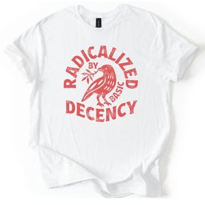Könnte beinhalten: Weißes T-Shirt mit roter Grafik. Die Grafik zeigt einen Vogel, der einen Zweig hält, umgeben von den Worten "RADICALIZED BY BASIC DECENCY" in einem kreisförmigen Design. Das Shirt hat kurze Ärmel und einen Rundhalsausschnitt.