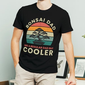 May include: A black t-shirt with a vintage-style graphic that says "Bonsai Dad Like a Regular Dad But Cooler". The graphic features a bonsai tree in a pot with a sunset background.