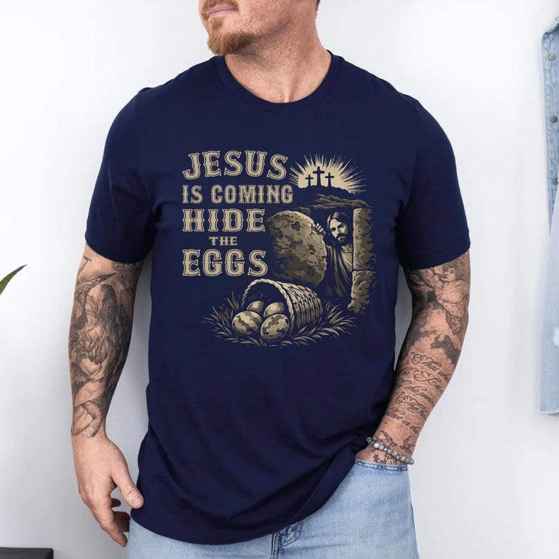 May include: Navy blue t-shirt with a graphic featuring Jesus emerging from a tomb, a basket of eggs, and the text "JESUS IS COMING HIDE THE EGGS" in a vintage style. The design includes three crosses.
