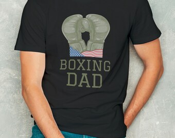 May include: Black t-shirt with a green and brown boxing glove graphic and an American flag. The text "BOXING DAD" is printed below the graphic.