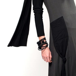K&ouml;nnte beinhalten: Ein graues Kleid mit einem schwarzen Stoffpanel und einem schwarzen Schal. Das Kleid hat einen langen &Auml;rmel und ein schwarzes Armband mit runden Perlen am Handgelenk.