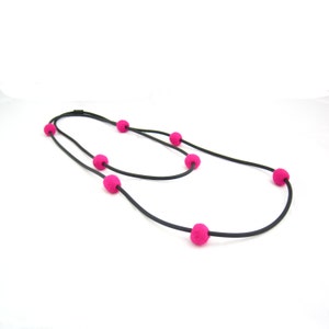 K&ouml;nnte beinhalten: Eine schwarze Schnurkette mit rosa Filzkugeln. Die Kette ist doppelf&auml;dig und hat sechs rosa Kugeln.