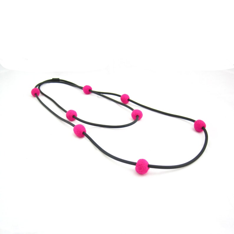K&ouml;nnte beinhalten: Eine schwarze Schnurkette mit rosa Filzkugeln. Die Kette ist doppelf&auml;dig und hat sechs rosa Kugeln.