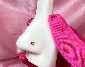 Puede incluir: Un modelo de piercing de nariz blanco con un aro de nariz de doble estrella de oro.