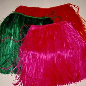 May include: Three hula skirts in bright colors, including a vibrant pink, a deep forest green, and a warm orange. Each skirt is constructed from thin, glossy synthetic strips attached to a braided waistband with long ties for securing.