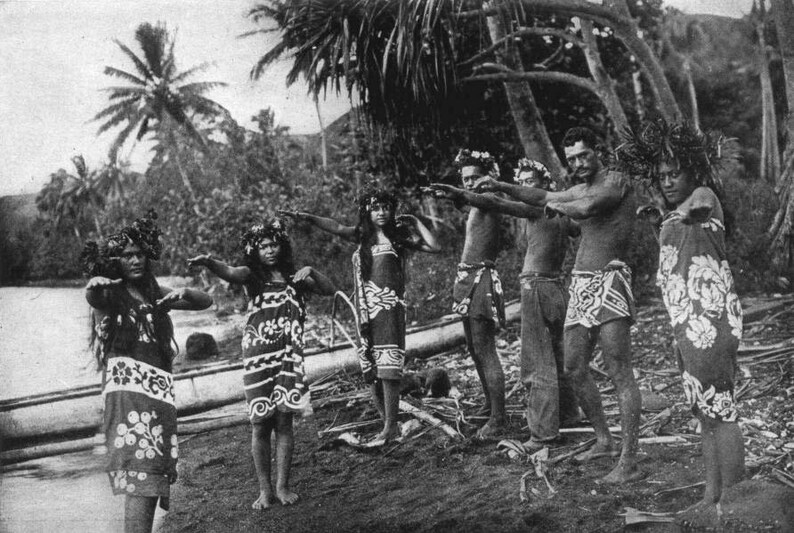 May include: Black and white photograph of a group of people in traditional attire, possibly performing a dance. The individuals are adorned with floral headpieces and patterned wraps, set against a tropical backdrop of palm trees and water.