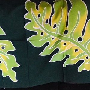 May include: Dark green fabric featuring a repeating pattern of large, stylized tropical leaves. The leaves are primarily light green with yellow and white accents, creating a vibrant contrast against the dark background. The design evokes a tropical or botanical theme.