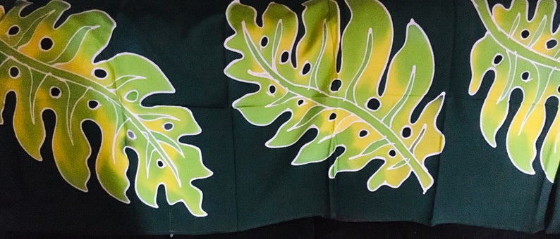 May include: Dark green fabric featuring a repeating pattern of large, stylized tropical leaves. The leaves are primarily light green with yellow and white accents, creating a vibrant contrast against the dark background. The design evokes a tropical or botanical theme.