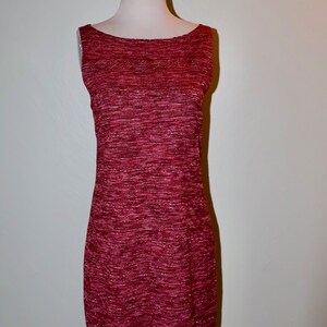 May include: A sleeveless, knee-length dress in a deep burgundy hue, displayed on a mannequin. The dress features a textured knit fabric with subtle metallic threads, creating a shimmering effect. The neckline is a simple scoop, and the dress has a fitted silhouette.